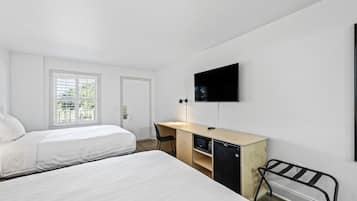 A hotel room with two beds, a desk with a microwave, a TV, and a window with blinds.