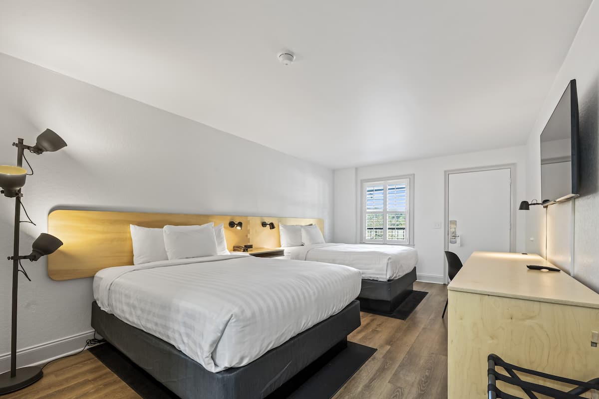 A modern hotel room with two beds, a desk, and a large mirror.