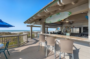 Una terraza con zona de bar, sillas y vista a la playa.