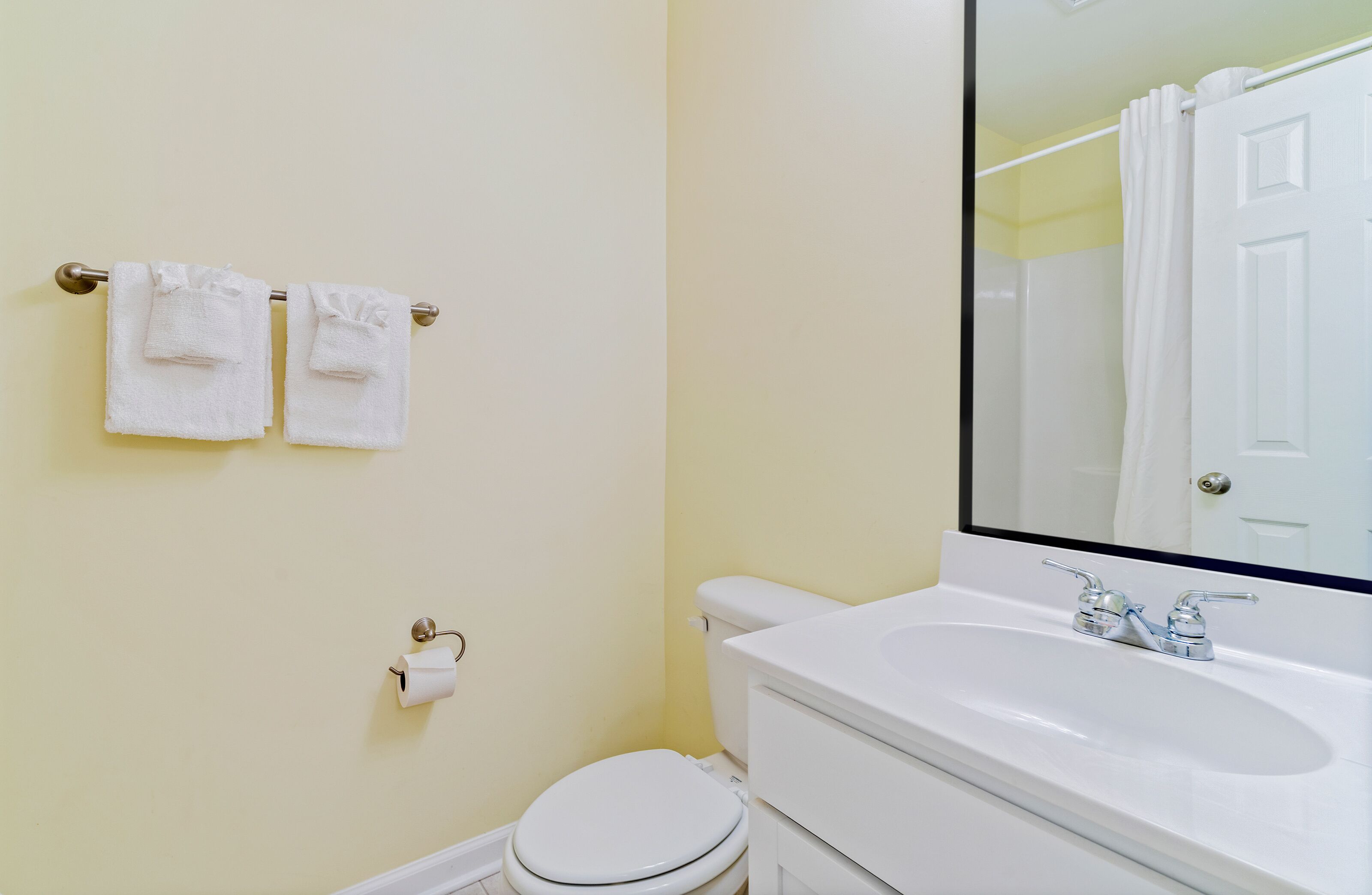 Baño con inodoro, lavamanos y dos toallas colgadas en un perchero.