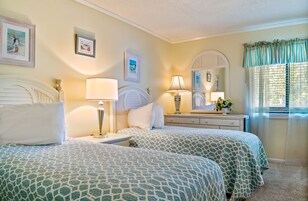 A bedroom with two beds, a nightstand, a dresser, and a window with curtains.