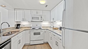 A modern kitchen with white cabinets, a stainless steel sink, a microwave, an oven, and a refrigerator. - Ocean Creek Resort (Myrtle Beach)