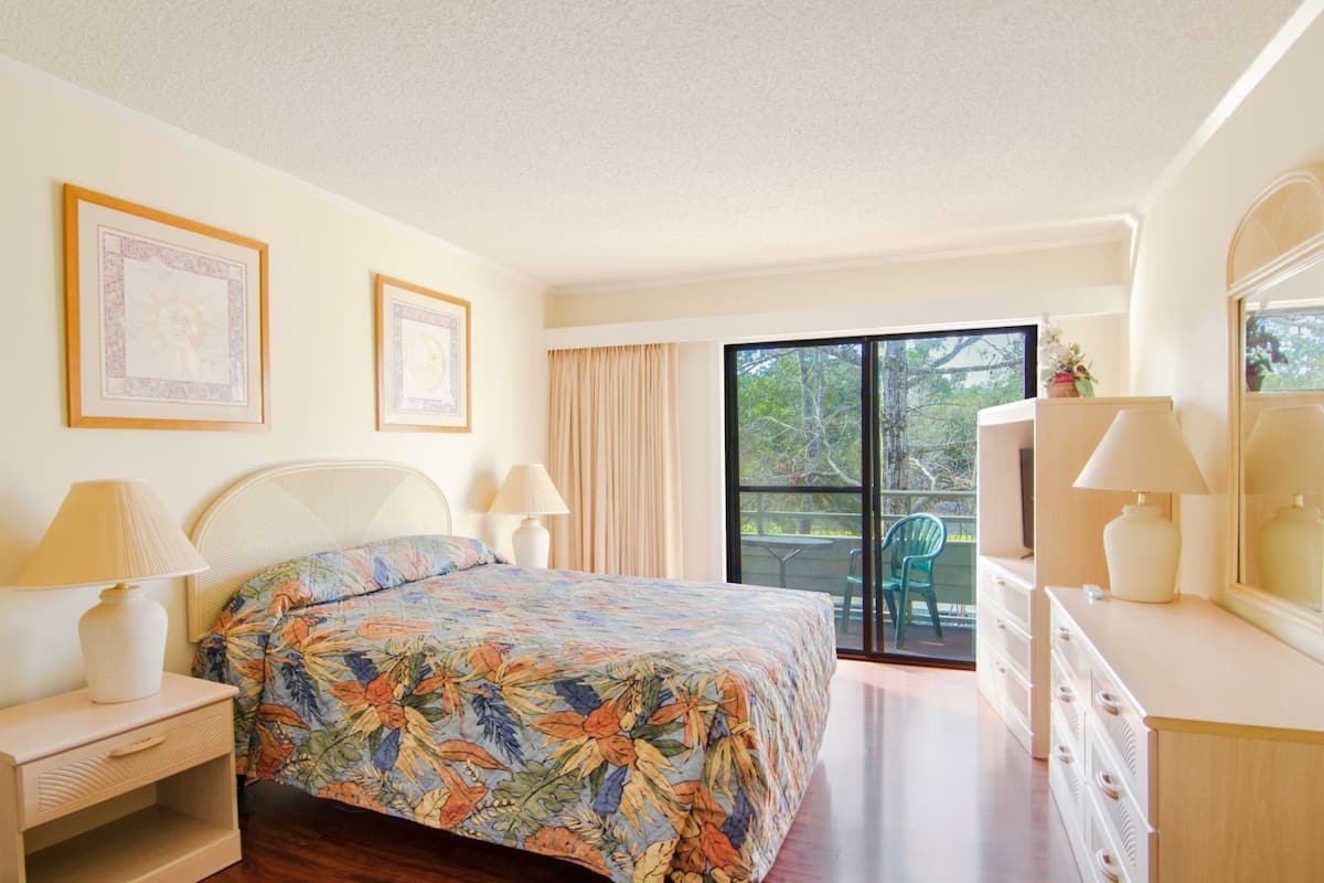 A bedroom with a bed, bedside lamps, a dresser, a window, and a balcony.