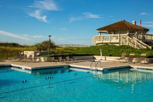 A swimming pool with lounge chairs and a building with a balcony and flag.