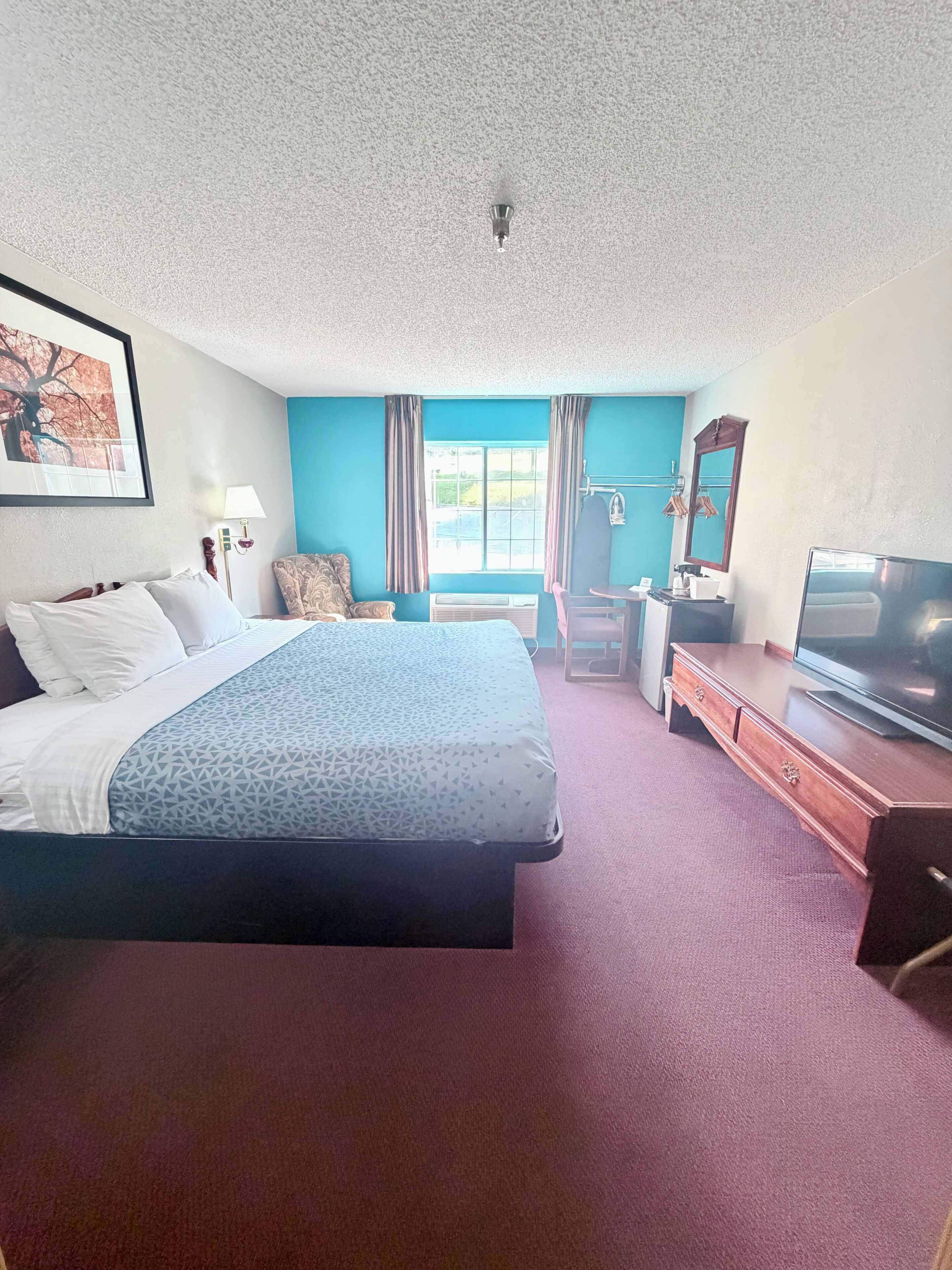 A hotel room with a bed, a desk, a television, and a window with curtains.