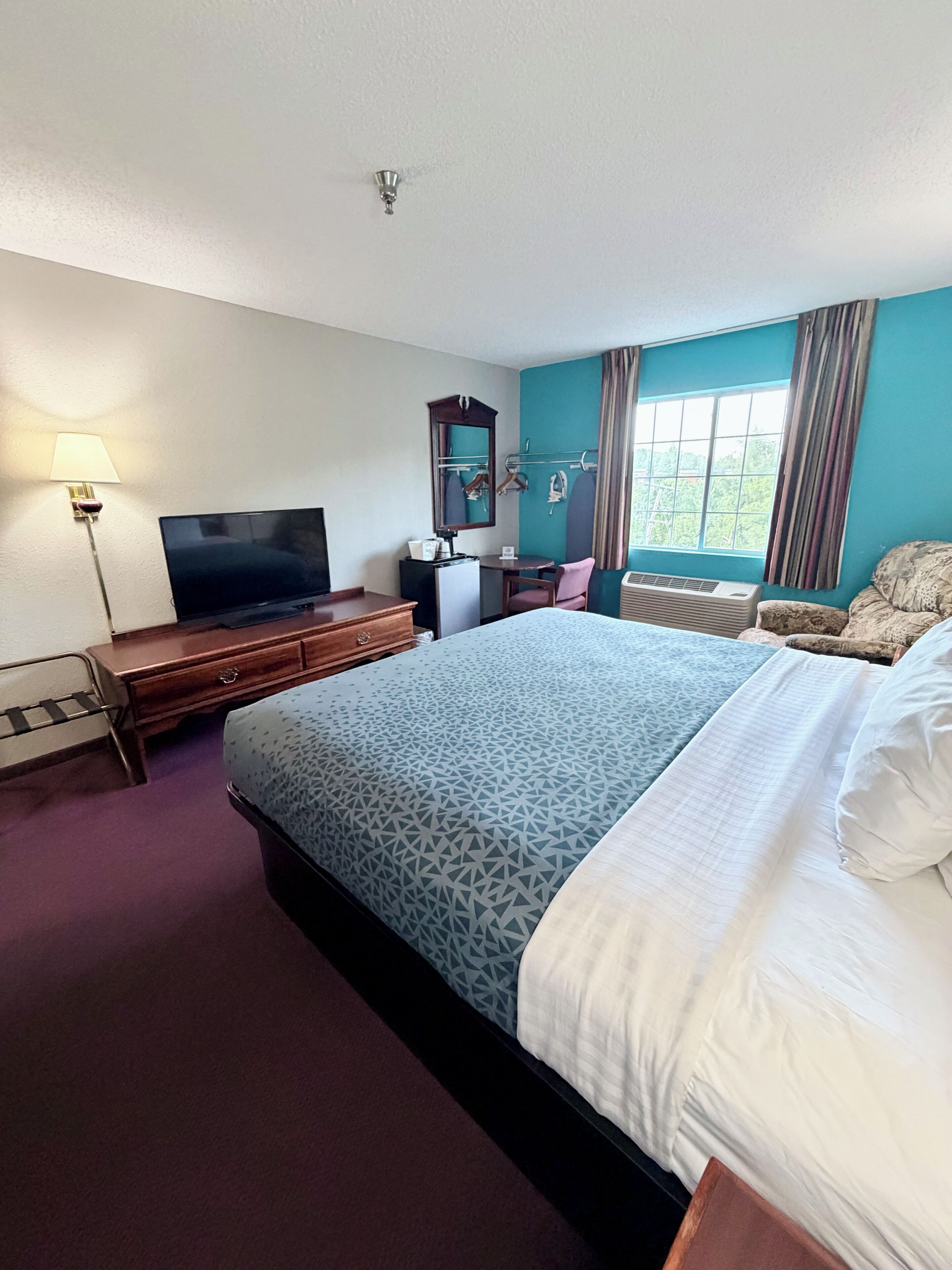 Une chambre d’hôtel équipée d’un lit, d’une télévision, d’un bureau, d’une chaise, d’un miroir et d’une fenêtre.