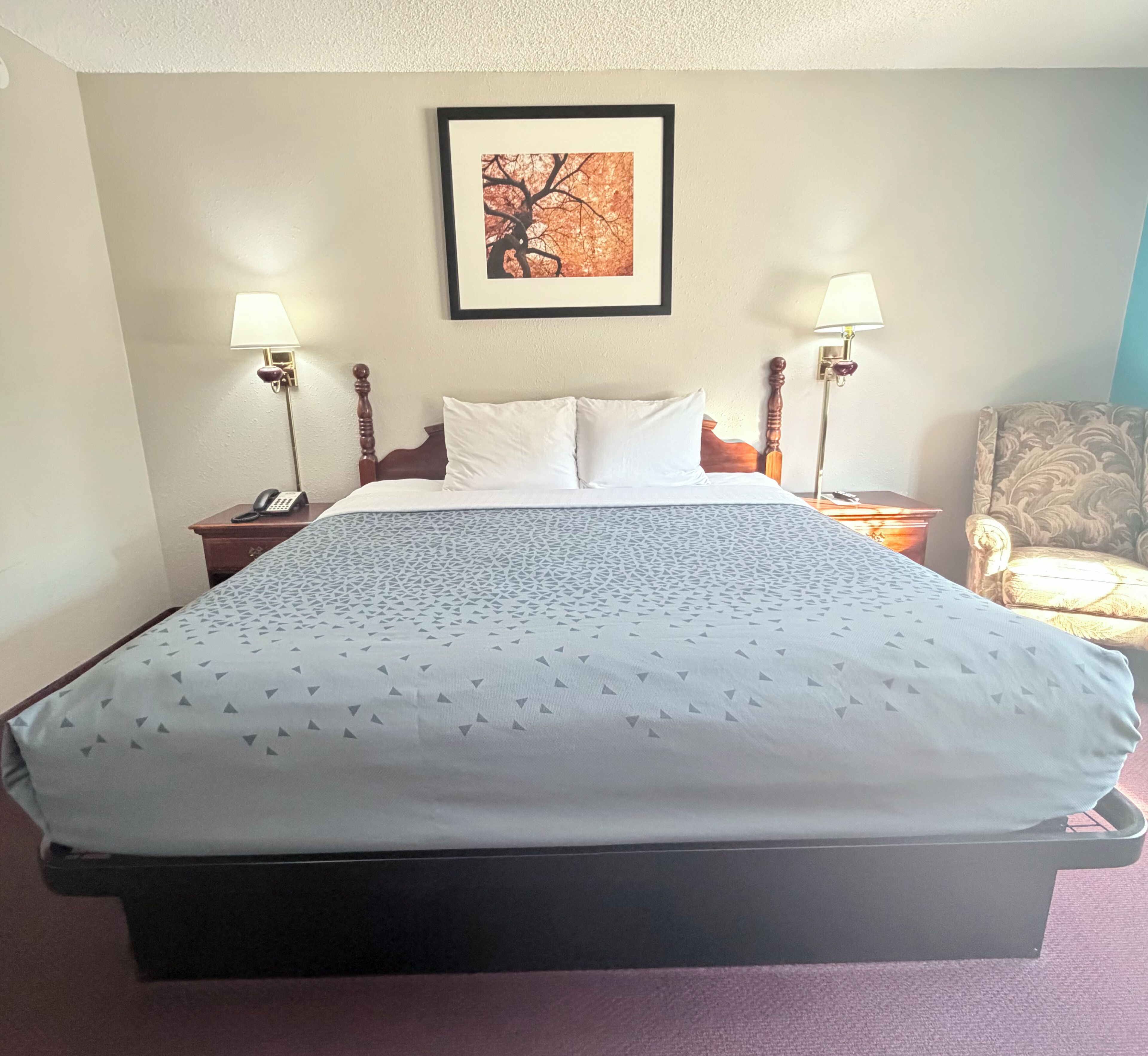 Una habitación de hotel con una cama grande, dos lámparas de noche, un cuadro en la pared y una silla.