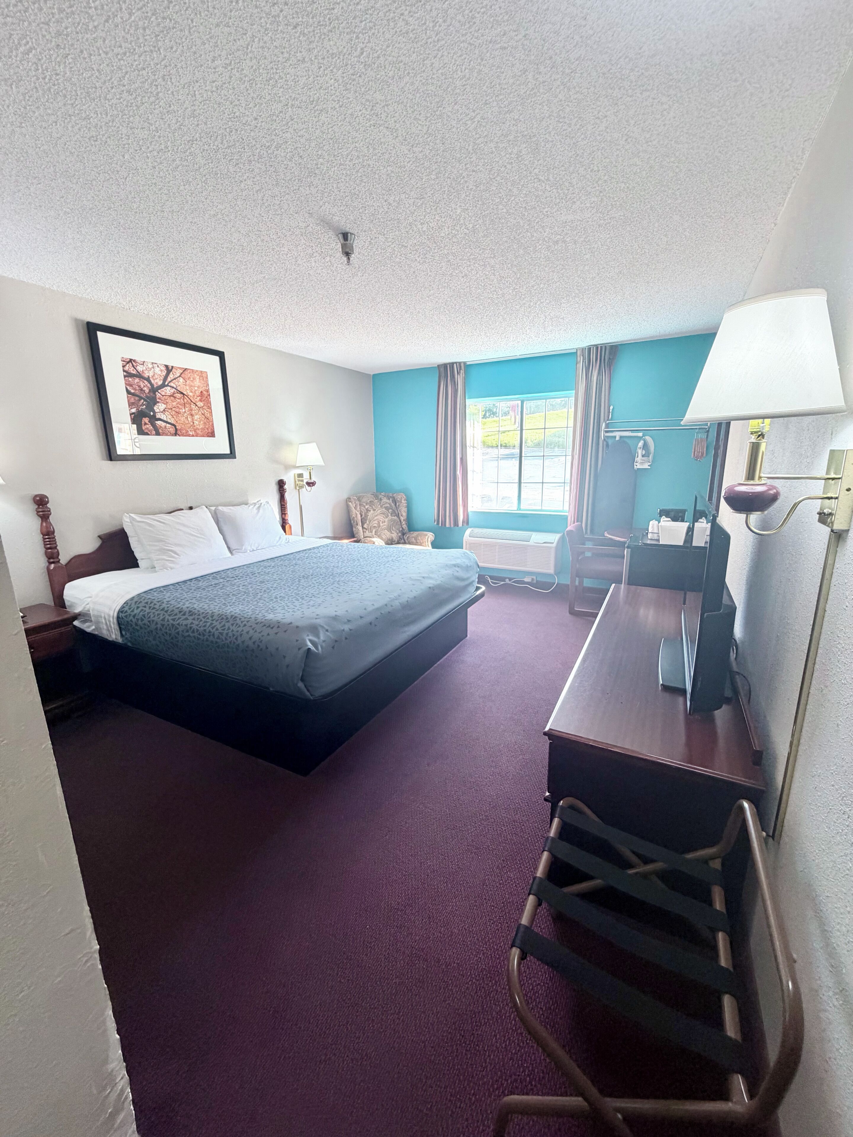 A hotel room with a bed, desk, chair, lamp, and a window with curtains.