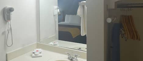 A hotel bathroom with a sink, mirror, and a hairdryer on the wall.