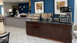 Et morgenmadsområde på et hotel med kaffemaskine, madbuffet, mikrobølgeovn og drikkemaskine.