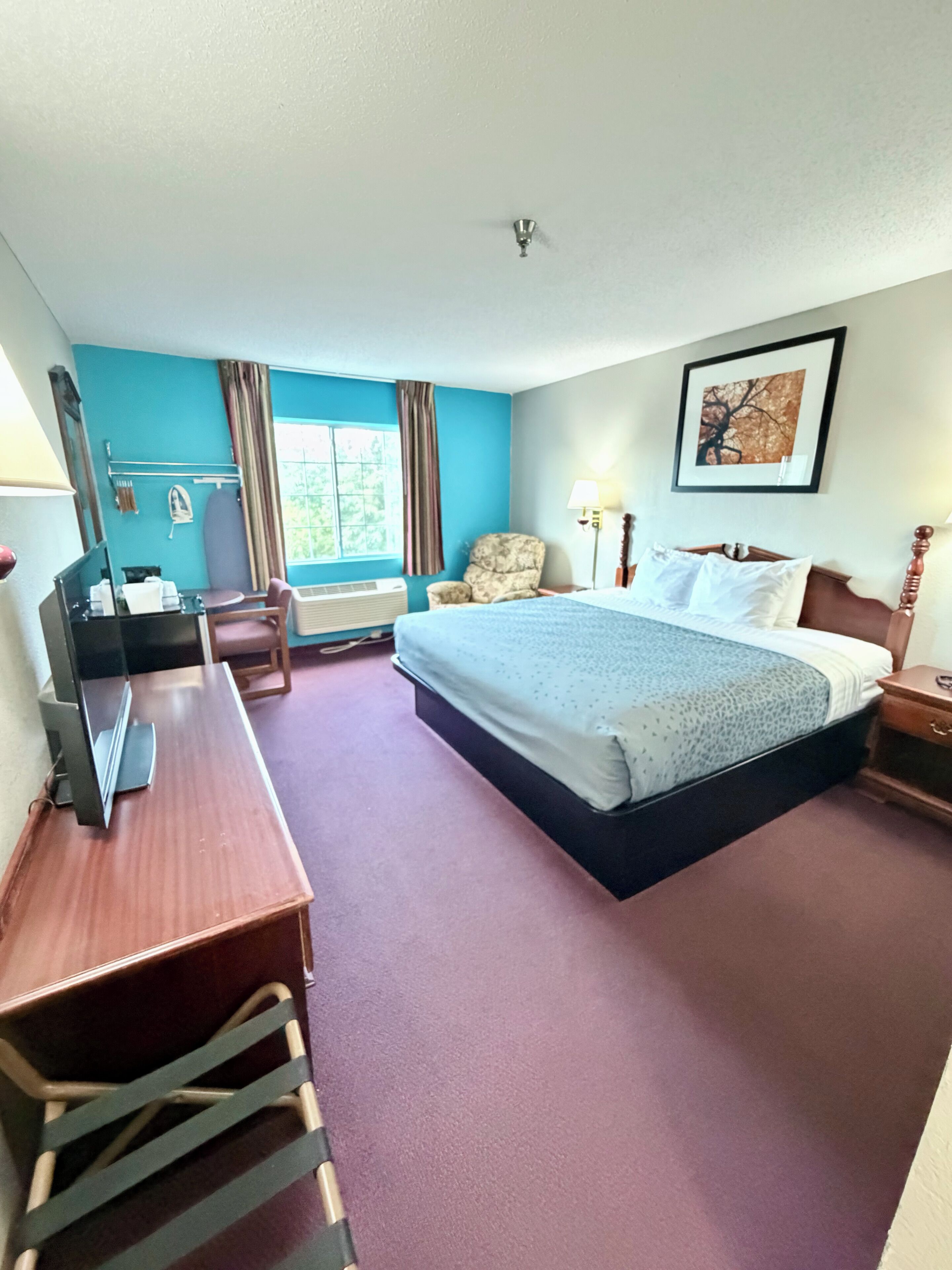 A hotel room with a bed, desk, chair, and a window with curtains.