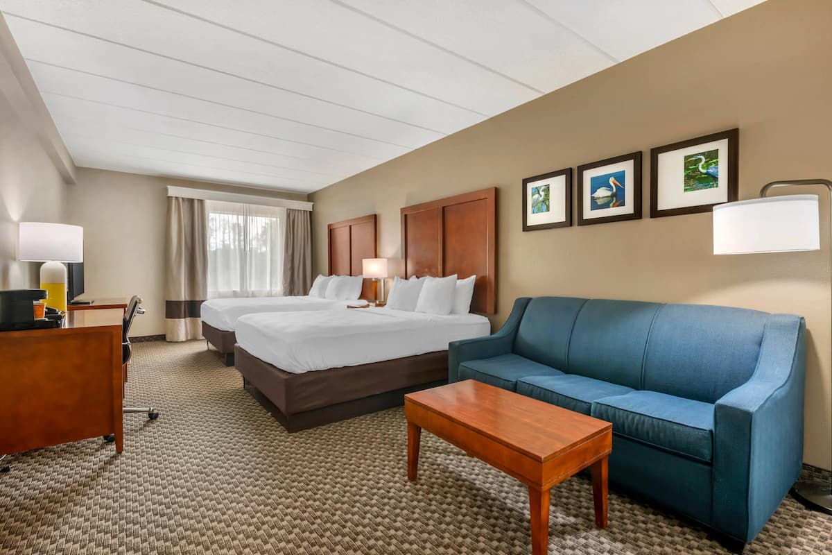 Ein Hotelzimmer mit zwei Betten, einem blauen Sofa, einem Holztisch und einem Schreibtisch mit Lampe.