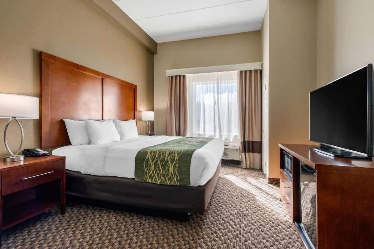 Ein Hotelzimmer mit Bett, Fernseher, Schreibtisch und einem Fenster mit Vorhängen.