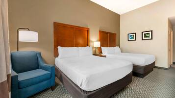 A hotel room with two beds, a blue armchair, a lamp, and two framed pictures on the wall.
