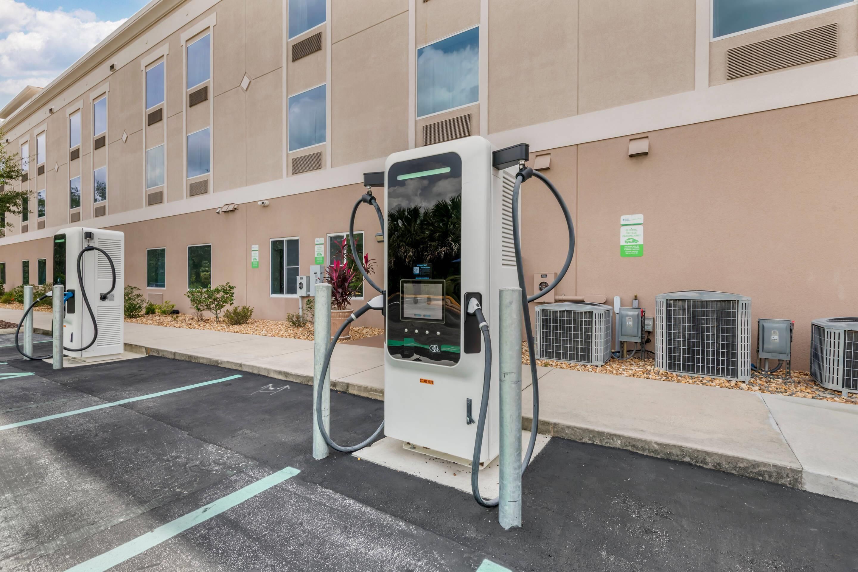 A parking area with electric vehicle charging stations, a building with multiple windows, and outdoor air conditioning units.