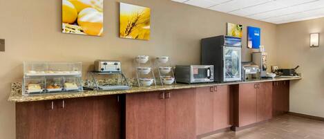 A hotel breakfast area with a counter, coffee machines, and a refrigerator.