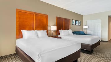 A hotel room with two beds, a wooden headboard, a nightstand with a lamp, and a door with a light switch.