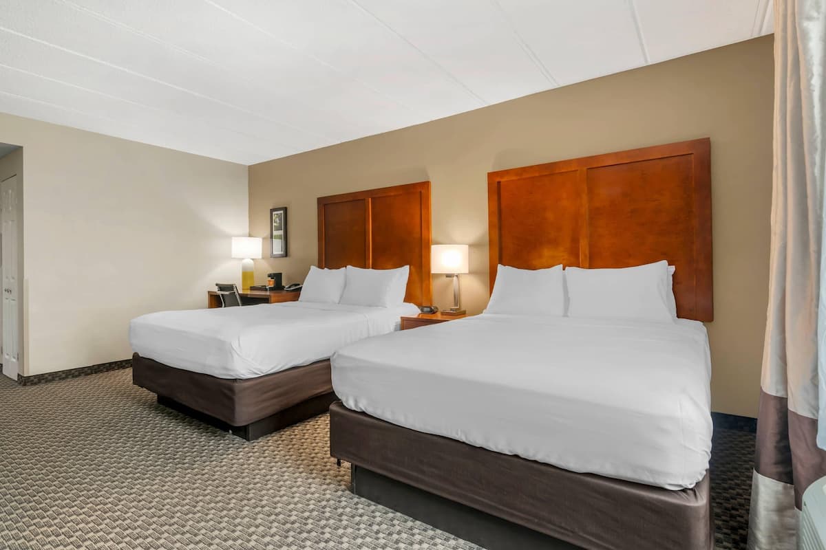Ein Hotelzimmer mit zwei Betten, Teppichboden und einem hölzernen Kopfteil.