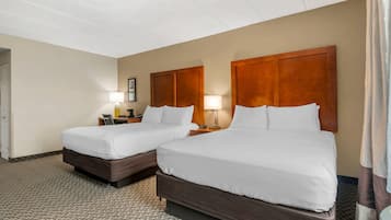 A hotel room with two beds, a carpeted floor, and a wooden headboard.