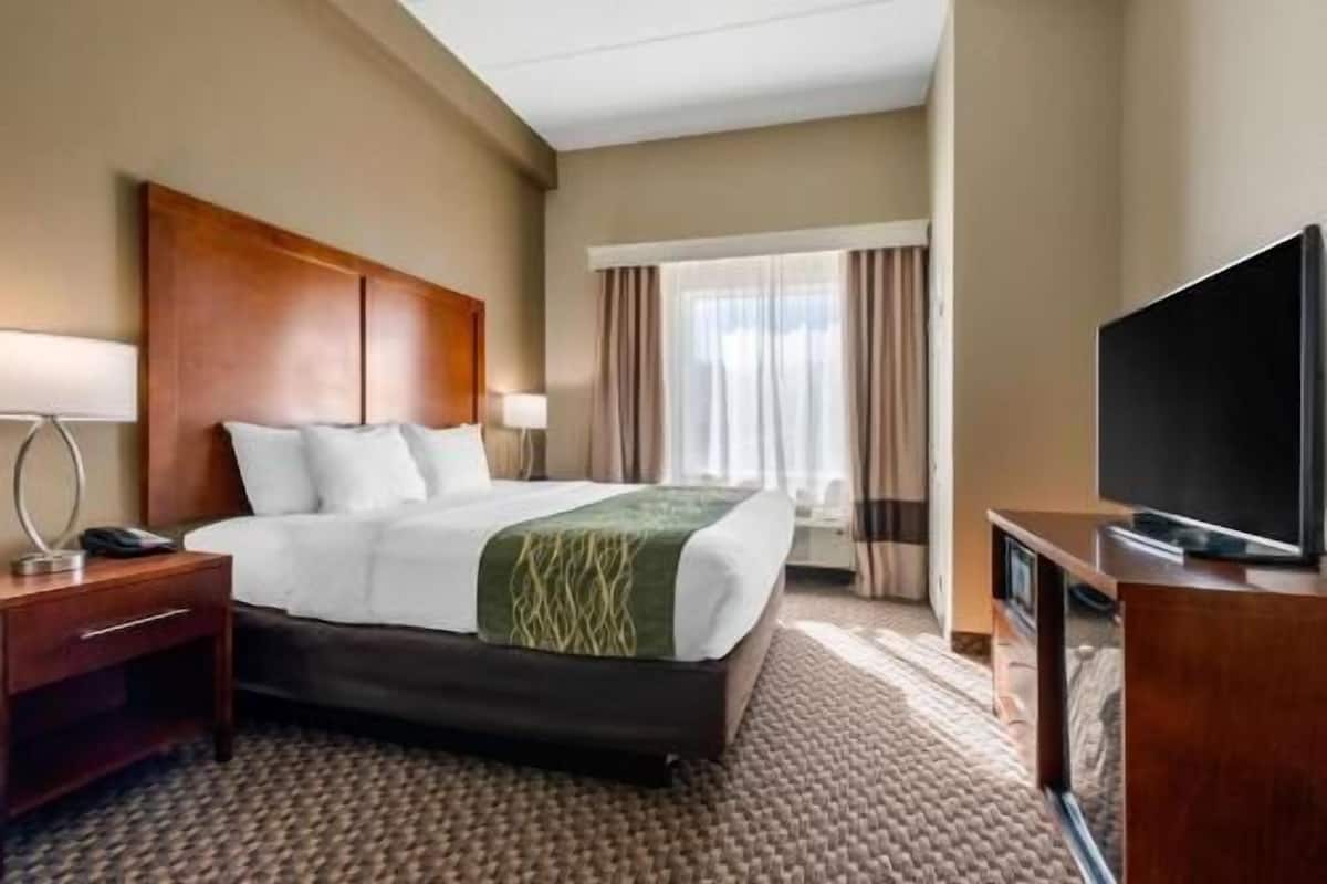 Ein Hotelzimmer mit Bett, Fernseher, Schreibtisch und einem Fenster mit Vorhängen.