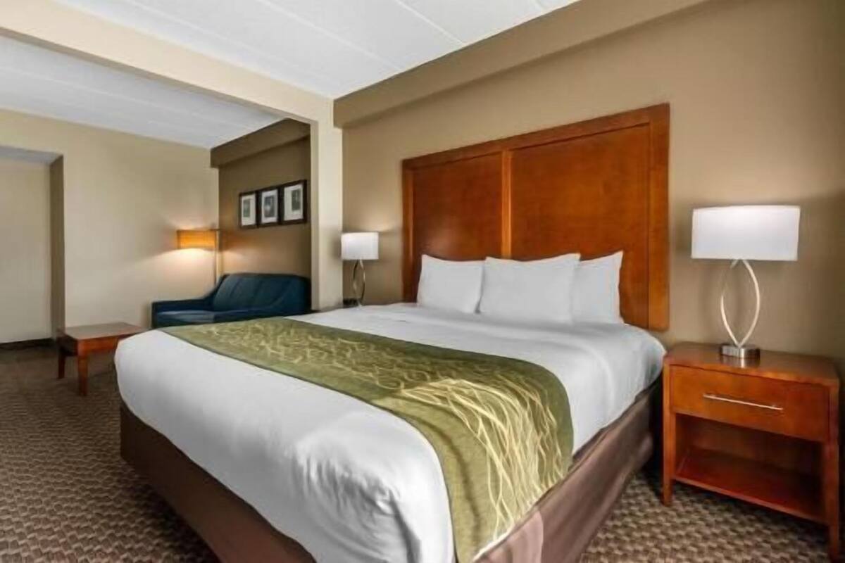 Ein Hotelzimmer mit einem großen Bett, zwei Nachttischen, einem Sessel und einem an der Wand befestigten Fernseher.
