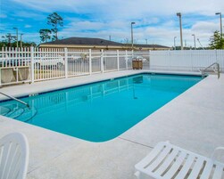 Una piscina rectangular con una cerca blanca y una silla blanca al frente.