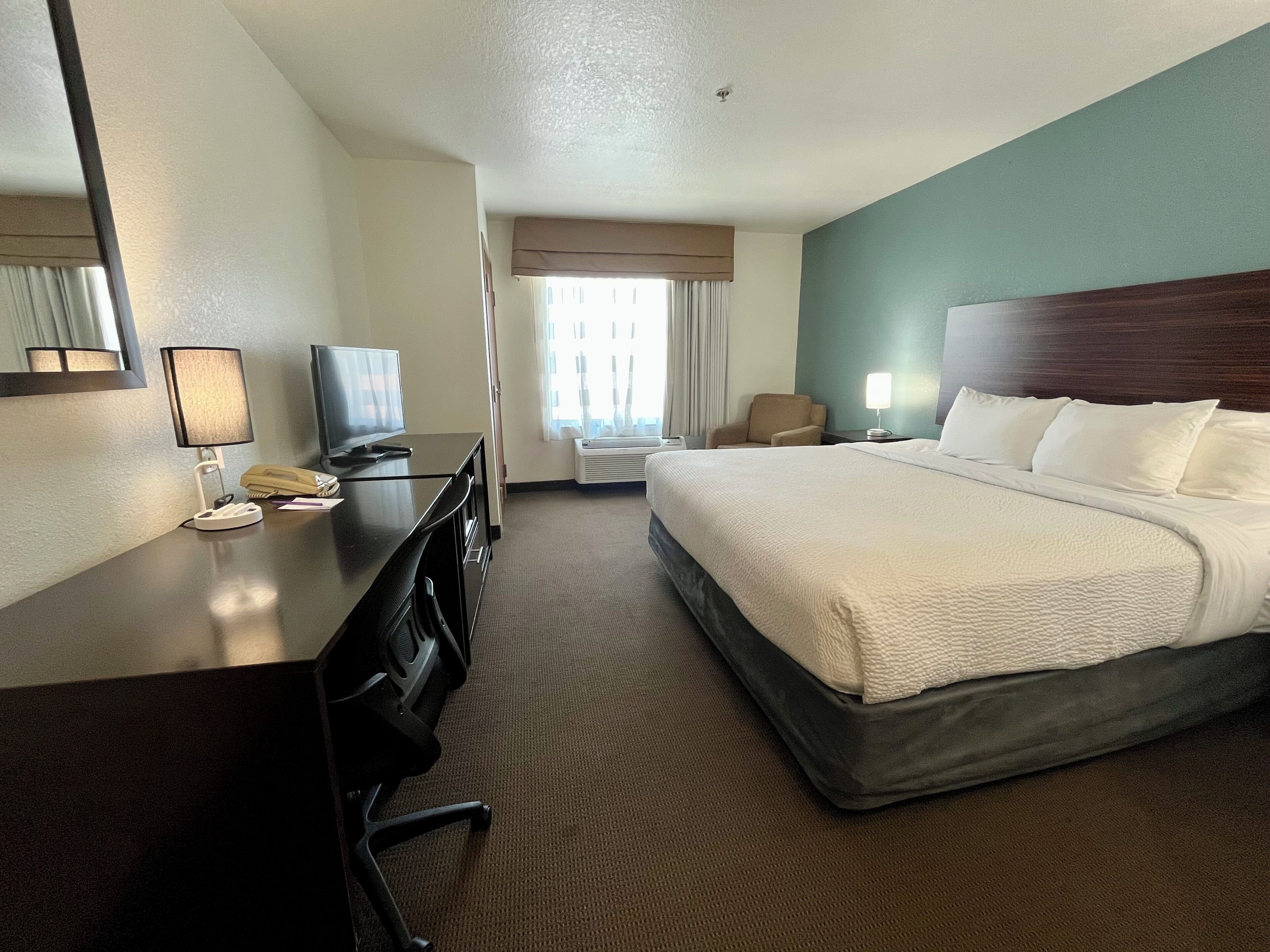 A hotel room with a bed, a desk with a computer and telephone, a chair, and a television.