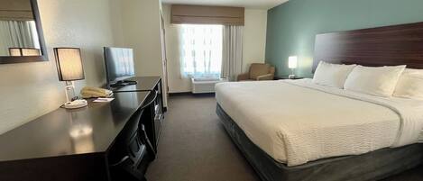 Habitación de hotel con cama, escritorio, computadora, teléfono, una silla y televisor.