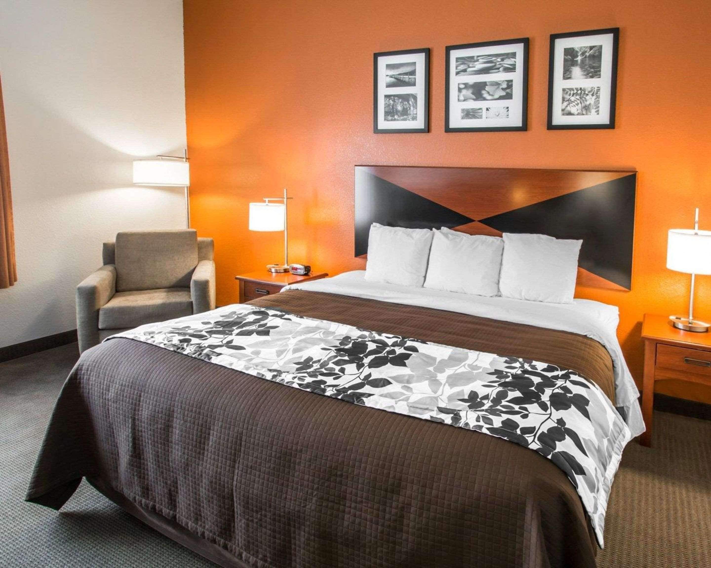 A hotel room with a large bed, a chair, two bedside tables with lamps, and a wall with framed pictures.