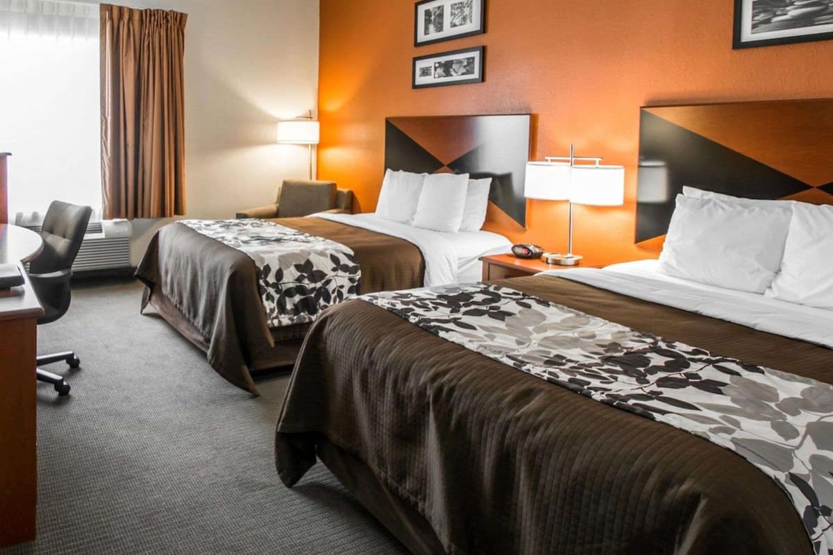 A hotel room with two beds, a desk, a chair, and a window with curtains.