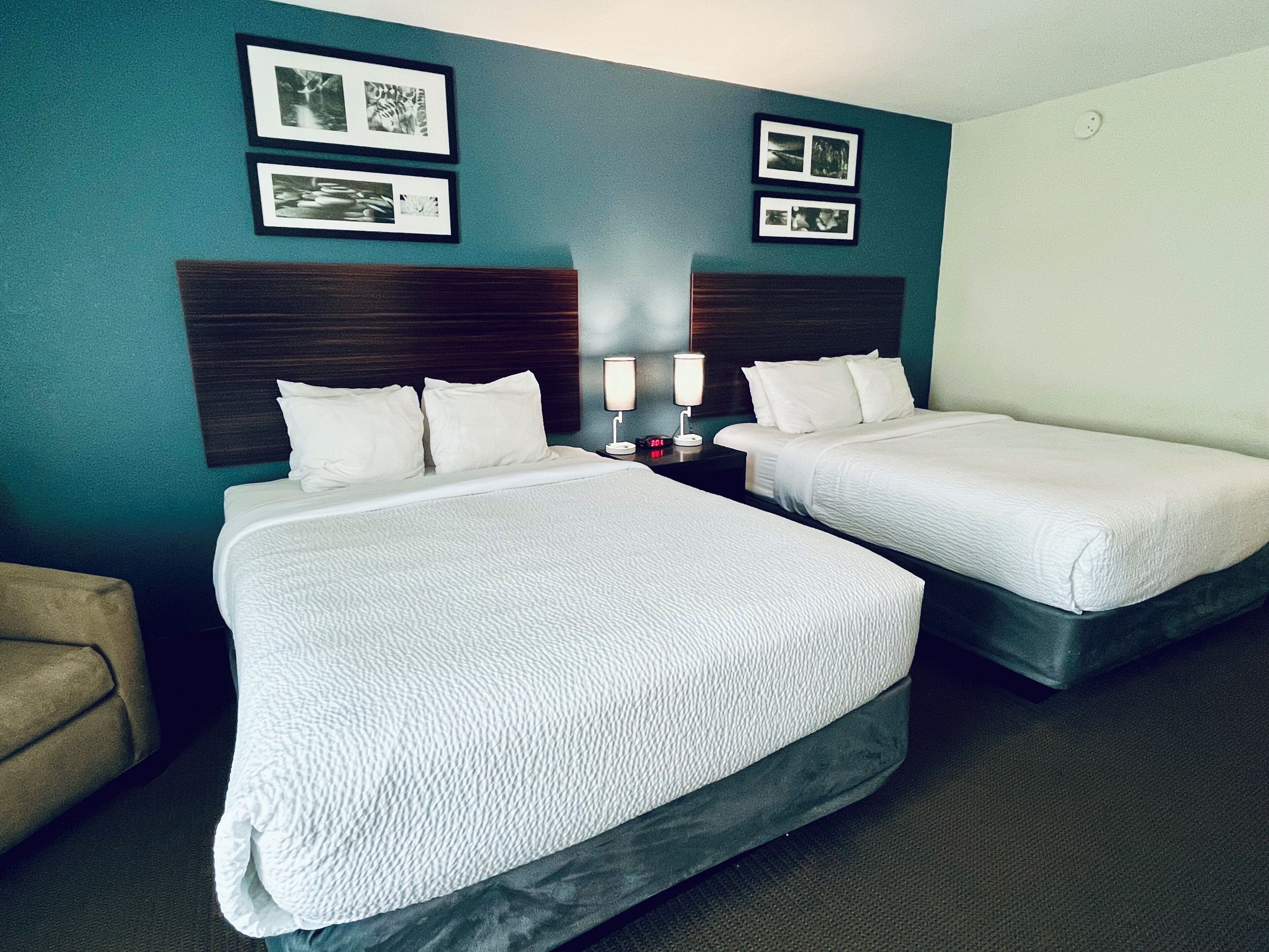 Habitación de hotel con dos camas, una mesita de noche con lámpara y cuadros en la pared.