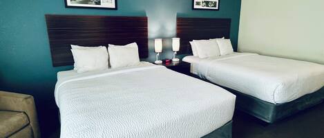 Habitación de hotel con dos camas, una mesita de noche con lámpara y cuadros en la pared.