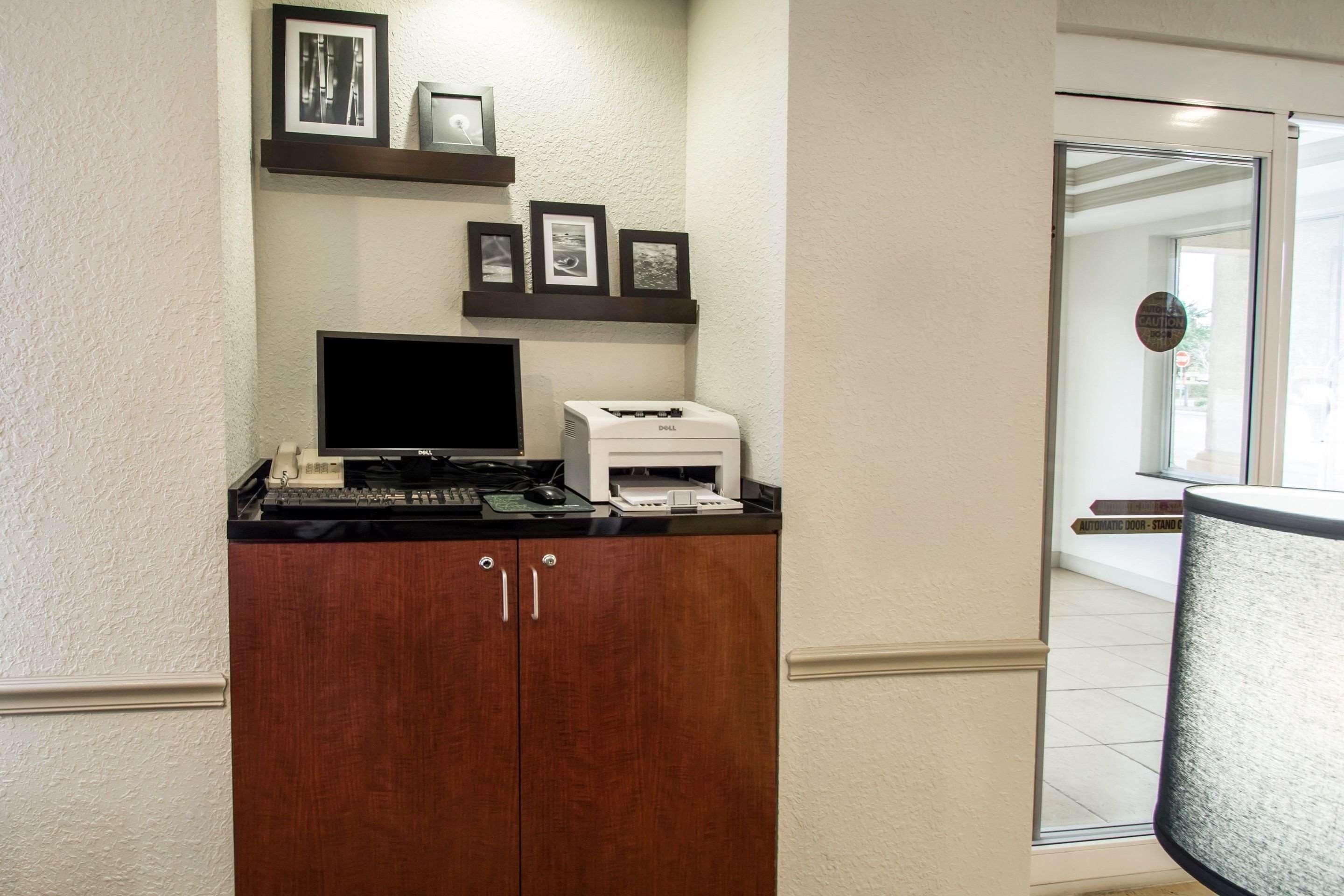 A desk with a computer, printer, and framed pictures on the wall.