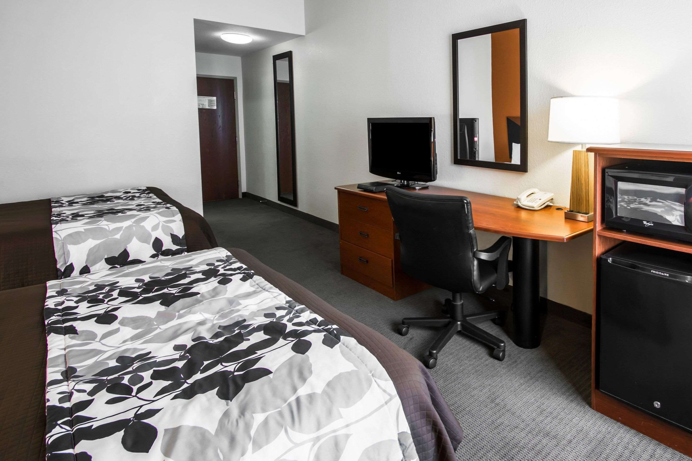 A hotel room with two beds, a desk with a computer, a chair, a telephone, and a refrigerator.