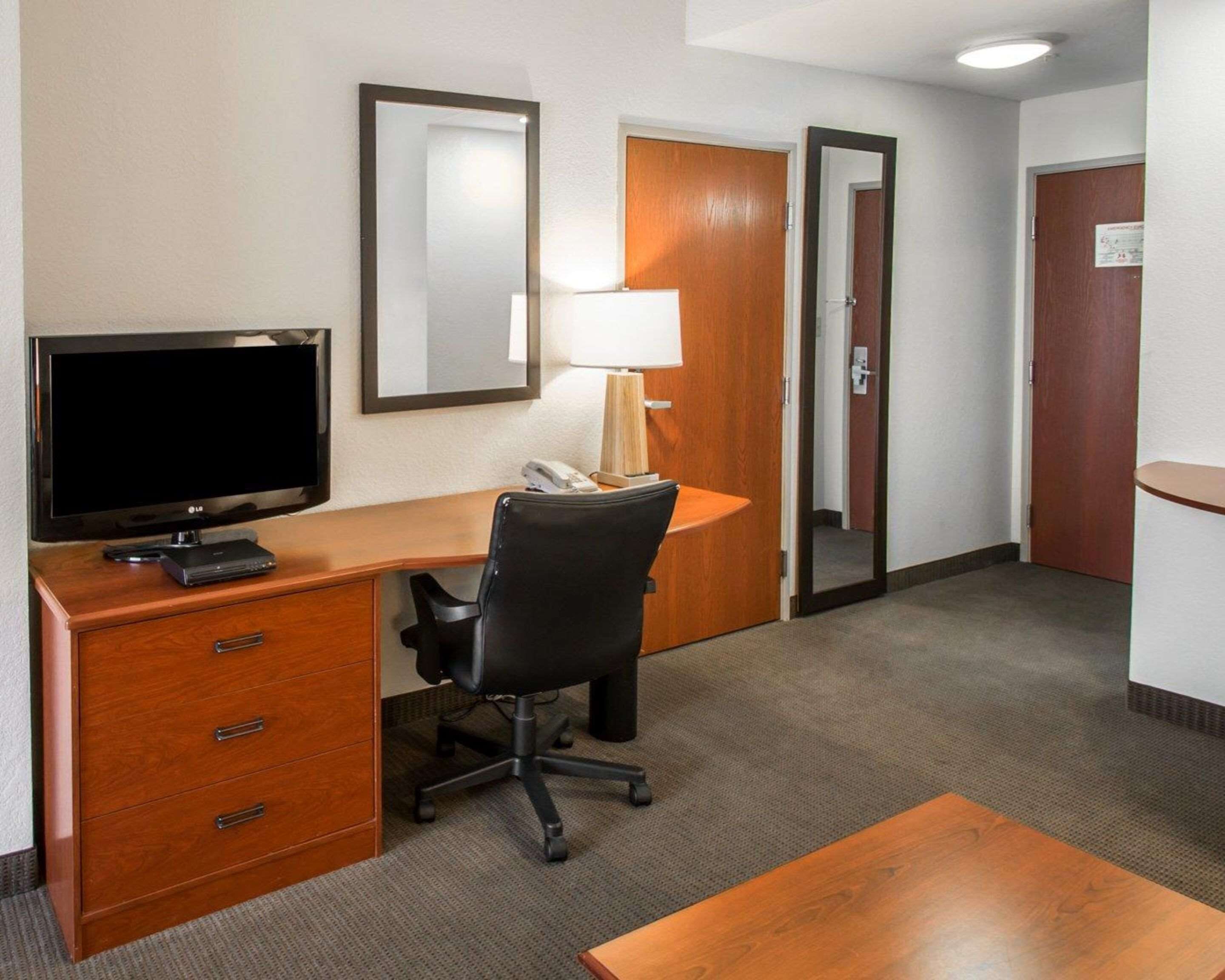 Habitación de hotel con un escritorio de madera, una silla de oficina negra, un televisor de pantalla plana, una lámpara y un teléfono.