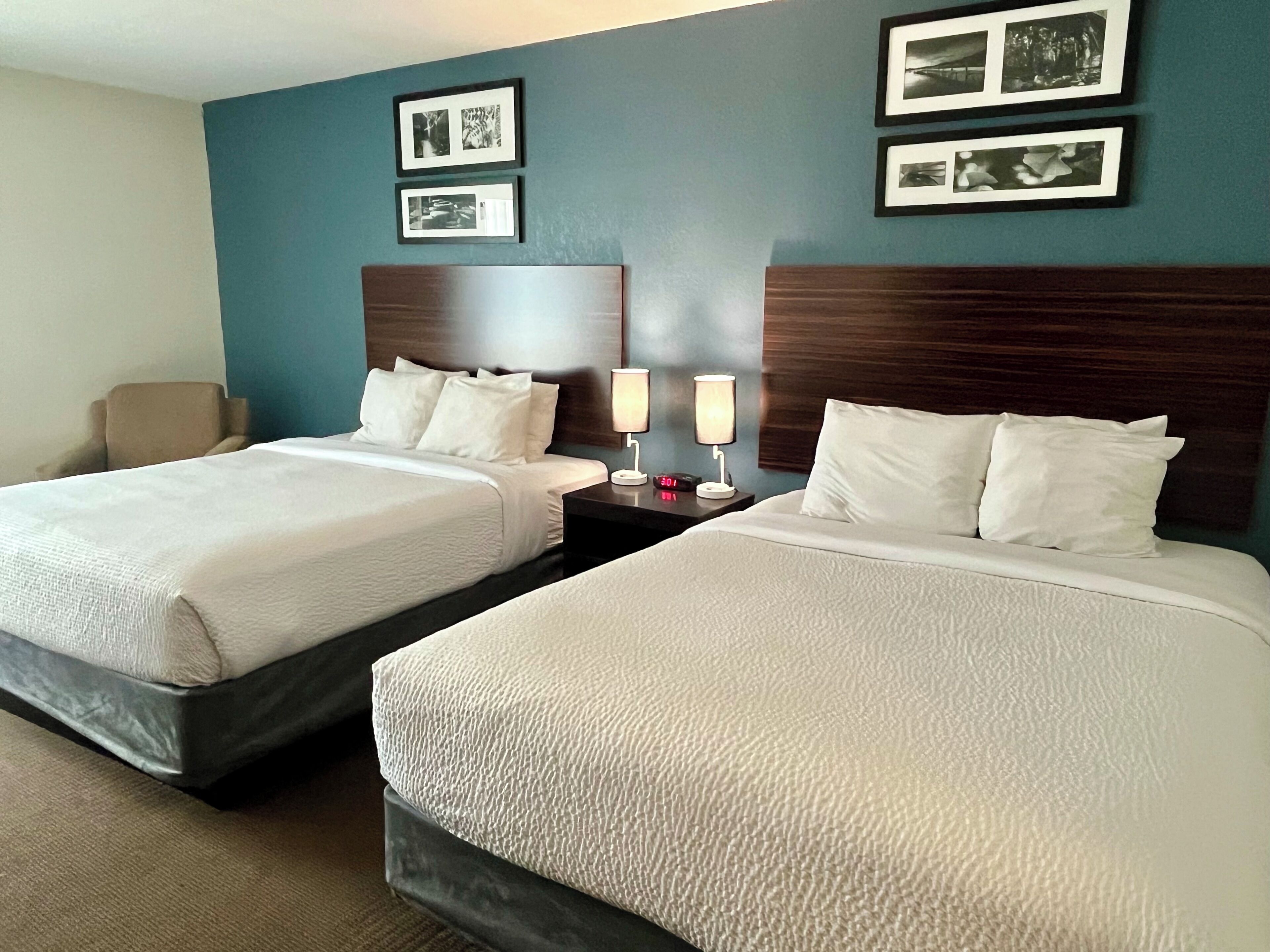 A hotel room with two beds, a nightstand with lamps, and framed pictures on the wall.