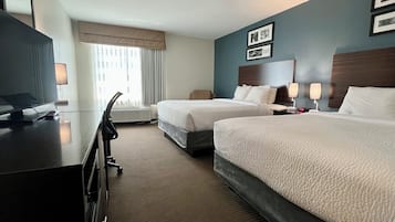 A hotel room with two beds, a desk with a computer, a chair, and a window with curtains.