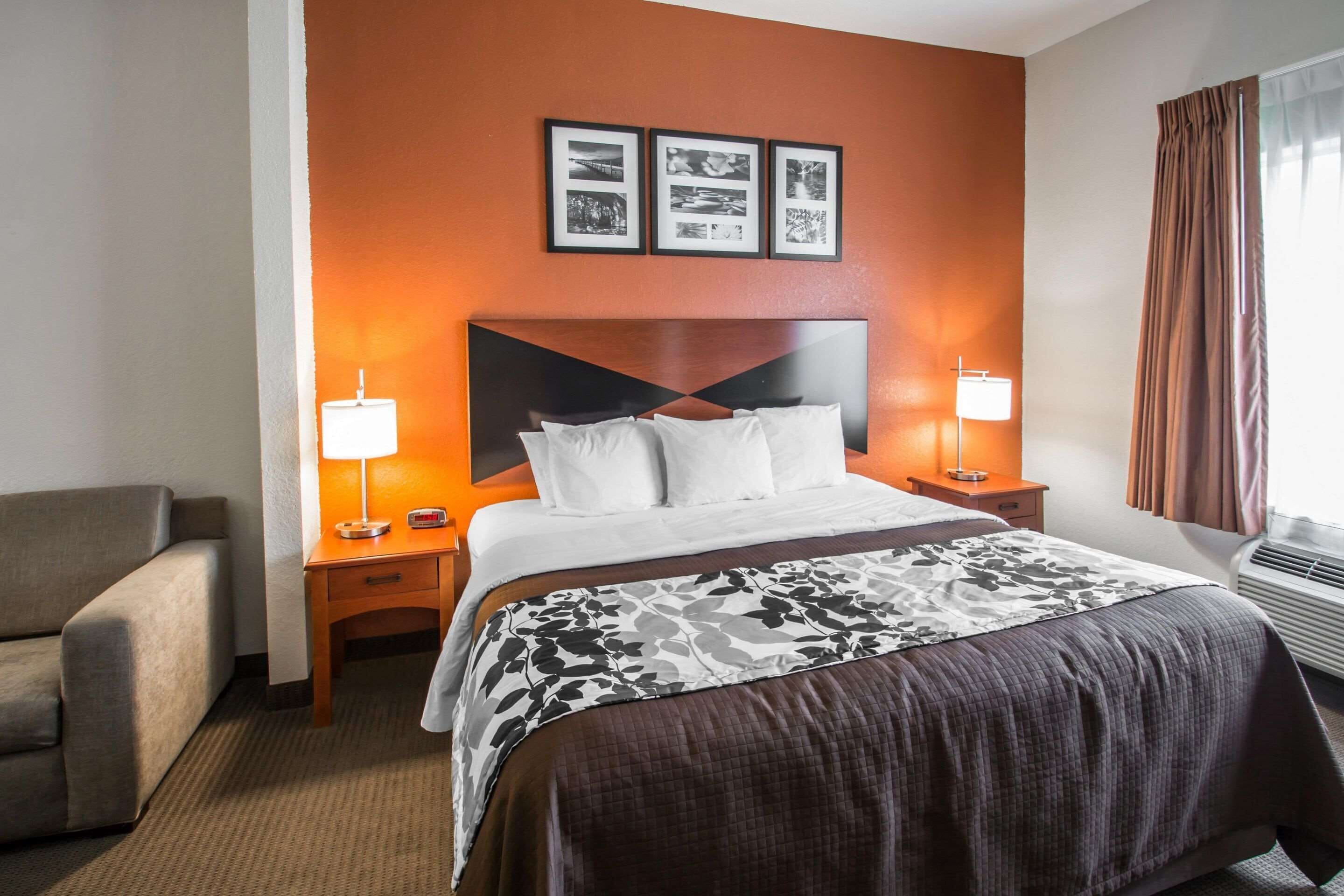 A hotel room with a bed, bedside tables, a lamp, a chair, and a wall with framed pictures.
