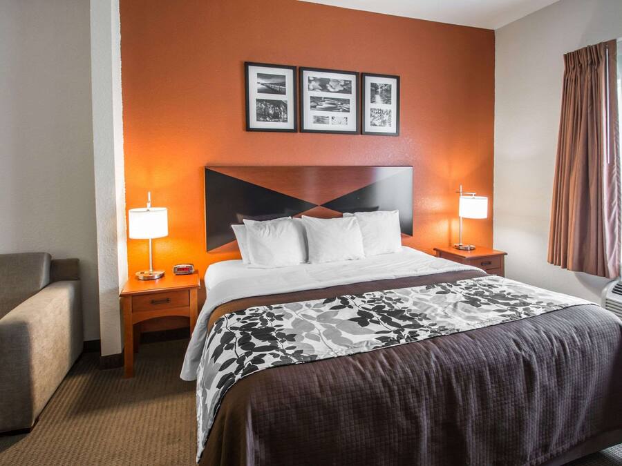 Una camera d'albergo con un letto, comodini, una lampada, una sedia e una parete con quadri.