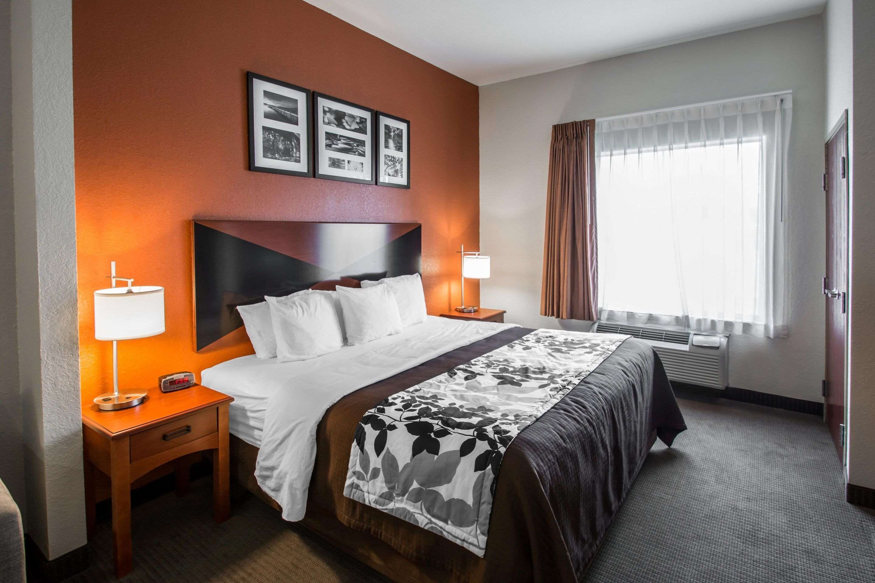 Une chambre d’hôtel avec un grand lit, deux tables de chevet avec des lampes, une fenêtre avec des rideaux et des tableaux encadrés au mur.