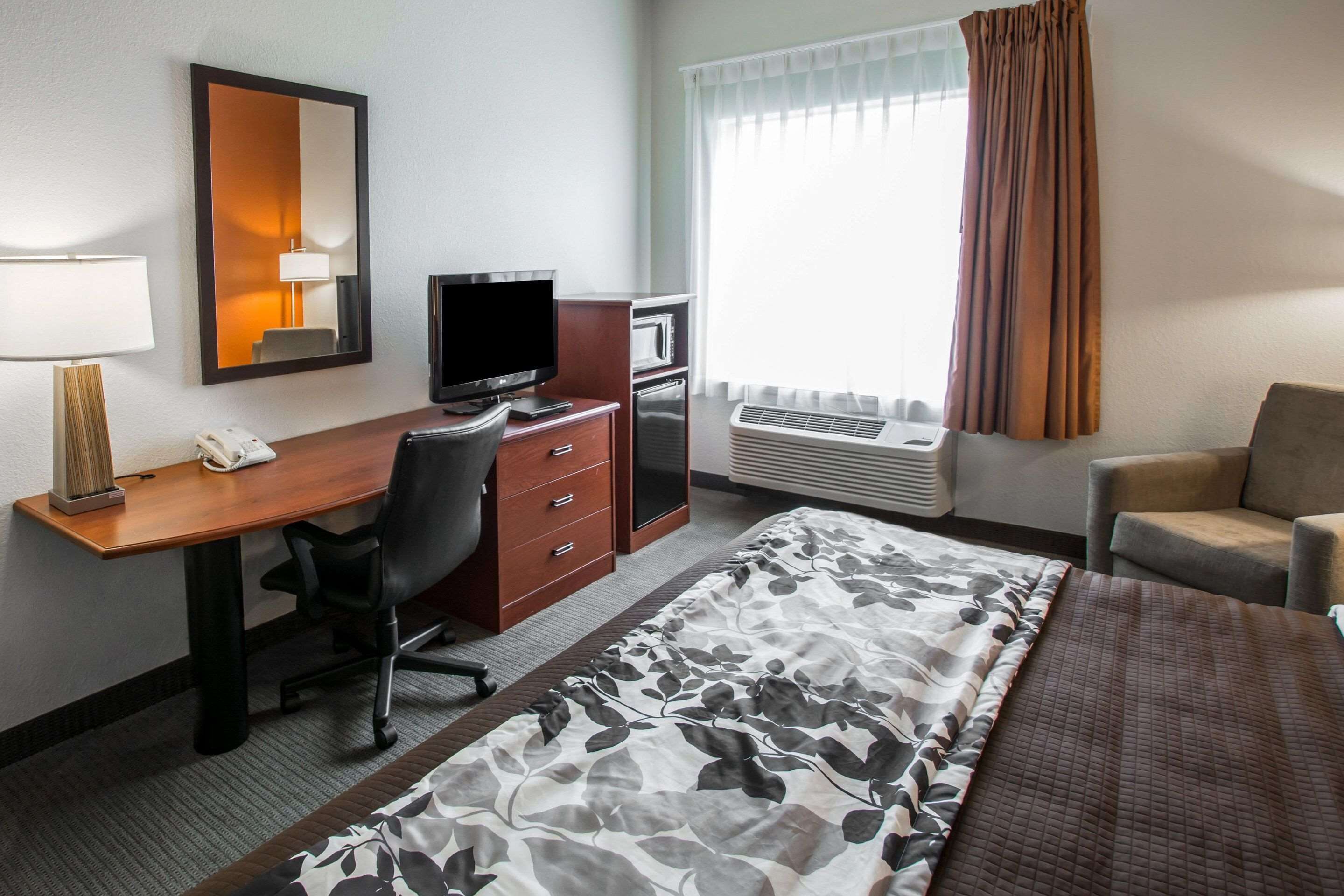 Una camera d'albergo con un letto, una scrivania con un computer, una sedia, una televisione, un telefono e una finestra con tende.