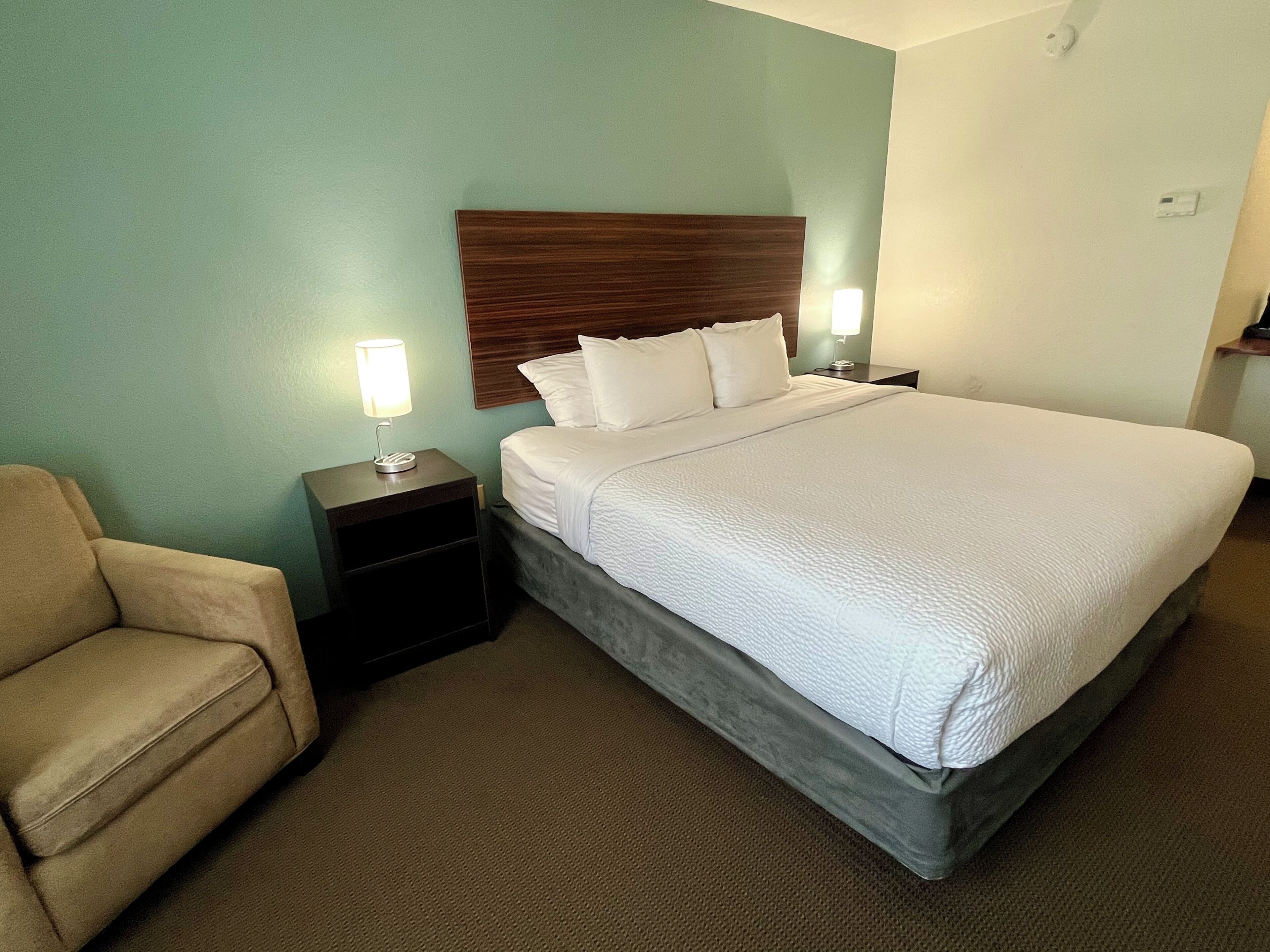 A hotel room with a bed, a nightstand, a lamp, and a chair.