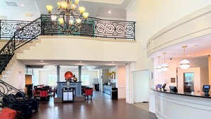 A spacious lobby with a grand staircase, a reception desk, and a chandelier.