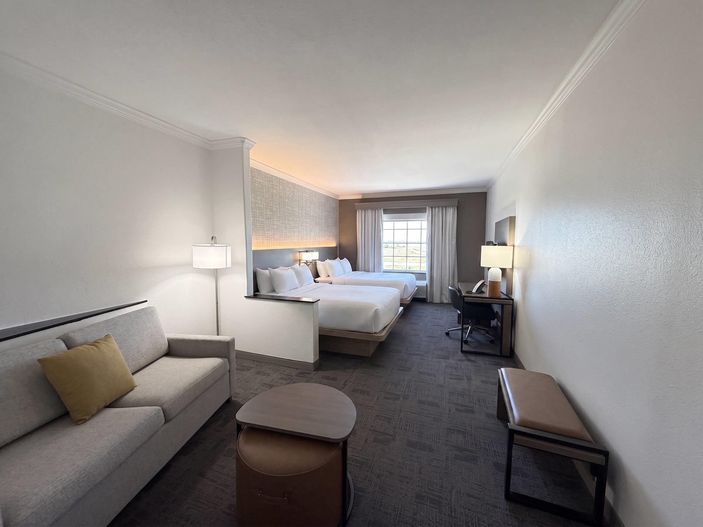 A hotel room with a sofa, two beds, a desk, and a chair.