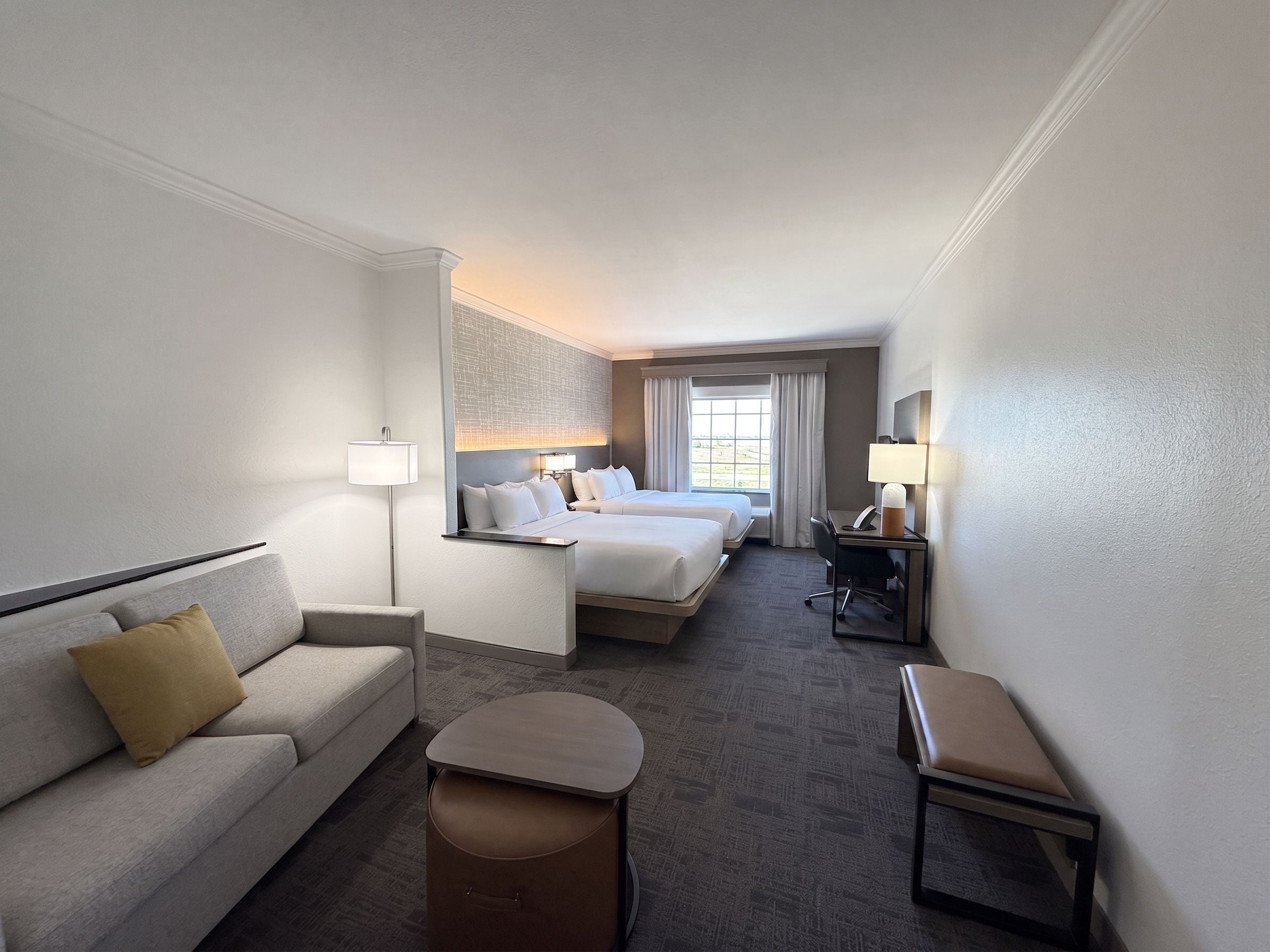 A hotel room with a sofa, two beds, a desk, and a chair.