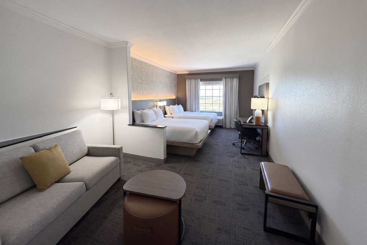Una habitación de hotel con sofá, dos camas, escritorio y una silla.