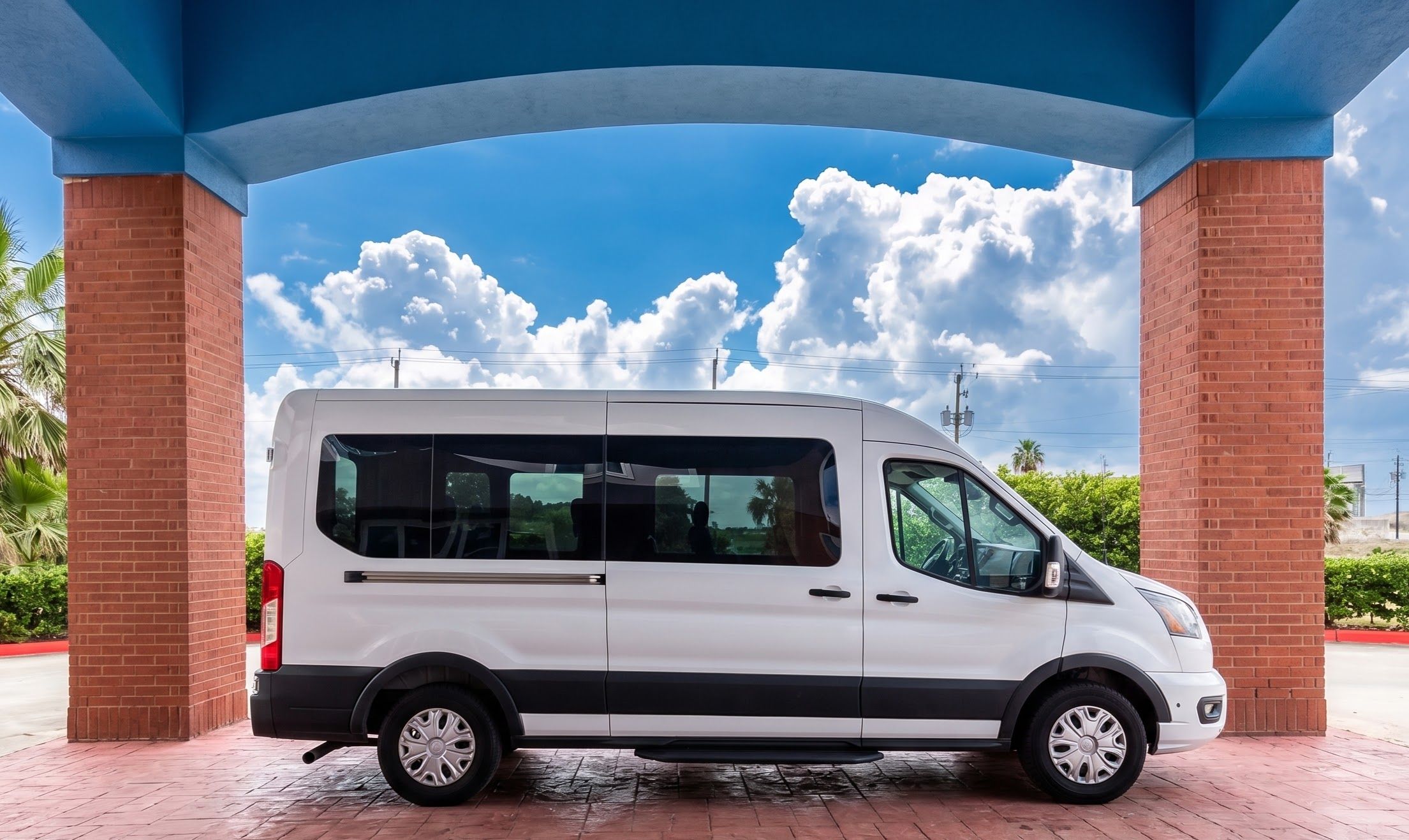 A white van parked under a blue structure with brick pillars, with a clear sky and clouds in the background.