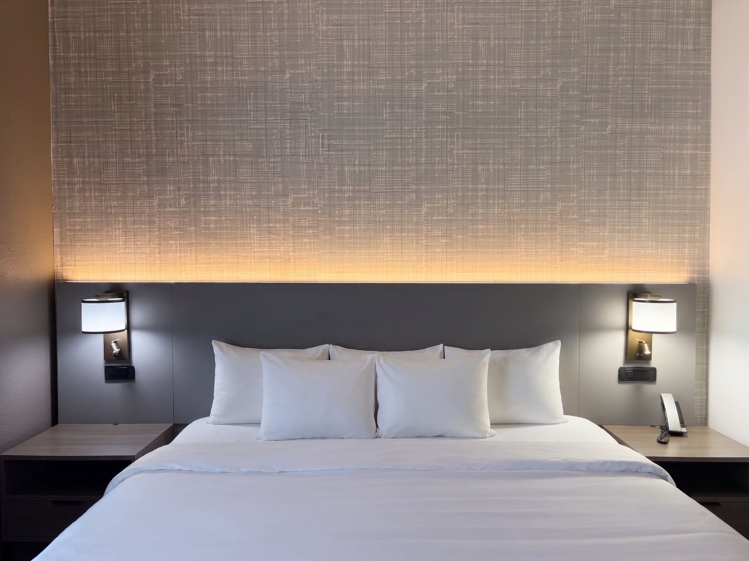 Una habitación de hotel con una cama grande, dos mesitas de noche y lámparas de pared.