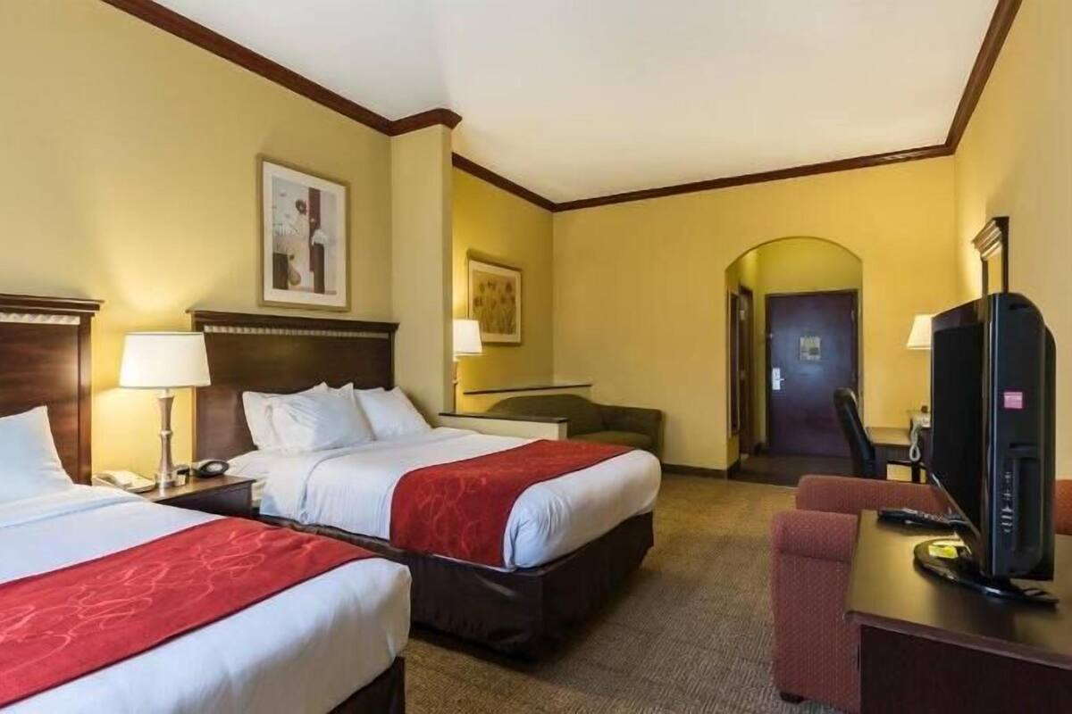 Habitación de hotel con dos camas, un escritorio con computadora y televisión.