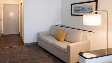Quarto de hotel com sofá, luminária, quadro na parede e piso de madeira.